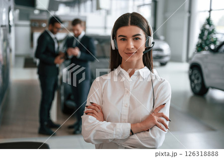Woman in headphones is in front of her colleagues. Three people are working together in the car showroom 126318888