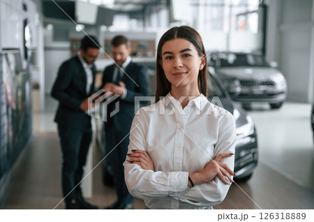 Woman is standing in front of her colleagues. Three people are working together in the car showroom 126318889
