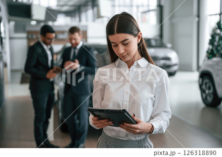 Woman is standing in front of her colleagues. Three people are working together in the car showroom 126318890