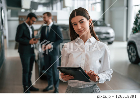 Woman is standing in front of her colleagues. Three people are working together in the car showroom 126318891