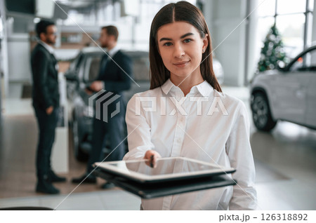 Woman is standing in front of her colleagues. Three people are working together in the car showroom 126318892