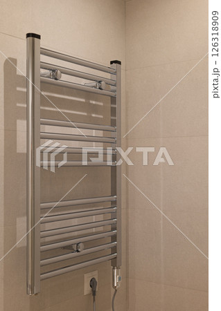 Wall mounted chrome towel warmer with horizontal bars set against neutral tiled bathroom wall Wall mounted chrome towel warmer with horizontal bars set against neutral tiled bathroom wall 126318909