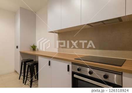 View of a modern kitchen with wood counter, white cabinets, oven, black stools and compact layout 126318924
