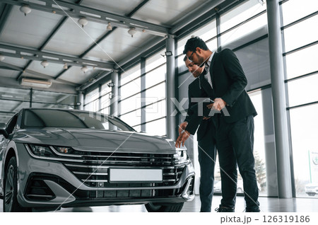 Business partners. Man is consulting the customer in the car showroom 126319186