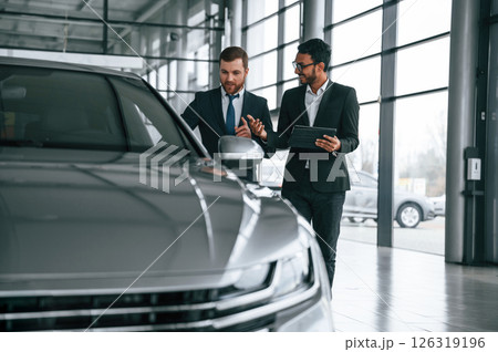 Checking quality of the vehicle. Man is consulting the customer in the car showroom Checking quality of the vehicle. Man is consulting the customer in the car showroom 126319196