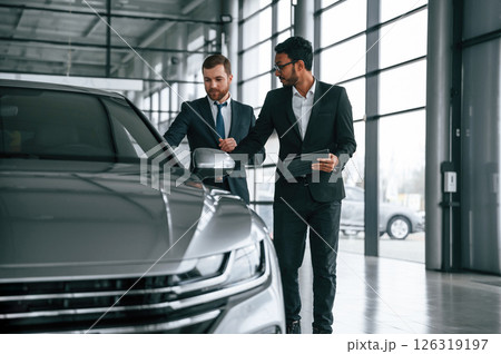 Checking quality of the vehicle. Man is consulting the customer in the car showroom Checking quality of the vehicle. Man is consulting the customer in the car showroom 126319197