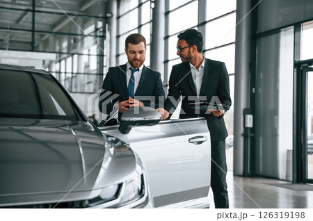 Checking quality of the vehicle. Man is consulting the customer in the car showroom Checking quality of the vehicle. Man is consulting the customer in the car showroom 126319198