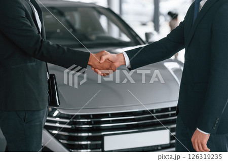 Close up view. Two businessmen are standing in the car showroom and making a deal, handshake Close up view. Two businessmen are standing in the car showroom and making a deal, handshake 126319235