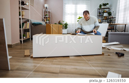 Man assembling furniture in bright, modern living room space Man assembling furniture in bright, modern living room space 126319350