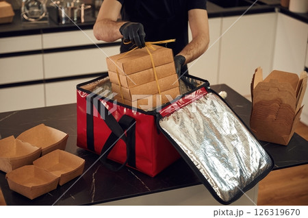 On the table. Man packs paper eco boxes into a bag for food delivery On the table. Man packs paper eco boxes into a bag for food delivery 126319670