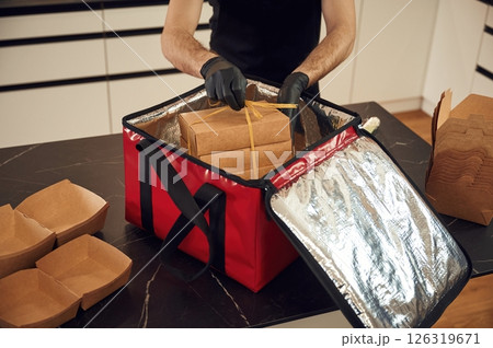 On the table. Man packs paper eco boxes into a bag for food delivery On the table. Man packs paper eco boxes into a bag for food delivery 126319671