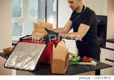 Focused on work. Man packs paper eco boxes into a bag for food delivery Focused on work. Man packs paper eco boxes into a bag for food delivery 126319672