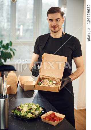 Holding and showing burgers and vegetables. Man is packing food into the paper eco boxes. Indoors, restaurant Holding and showing burgers and vegetables. Man is packing food into the paper eco boxes. Indoors, restaurant 126319680