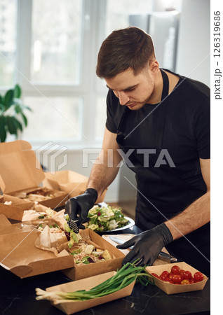 Adding vegetables to the burger. Man is packing food into the paper eco boxes. Indoors, restaurant Adding vegetables to the burger. Man is packing food into the paper eco boxes. Indoors, restaurant 126319686