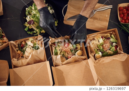 Delicious meal. Man is packing food into the paper eco boxes. Indoors, restaurant 126319697