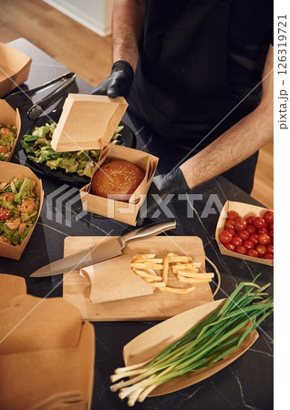 Opening the box with burger. Man is packing food. Indoors, restaurant Opening the box with burger. Man is packing food. Indoors, restaurant 126319721