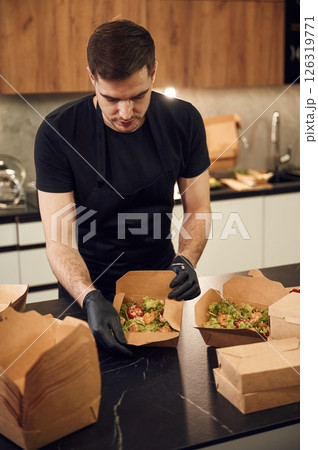 On the table. Man is packing food into the paper eco boxes. Indoors, restaurant 126319771