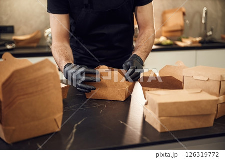 On the table. Man is packing food into the paper eco boxes. Indoors, restaurant On the table. Man is packing food into the paper eco boxes. Indoors, restaurant 126319772