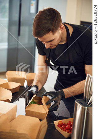 On the table. Man is packing food into the paper eco boxes. Indoors, restaurant 126319774