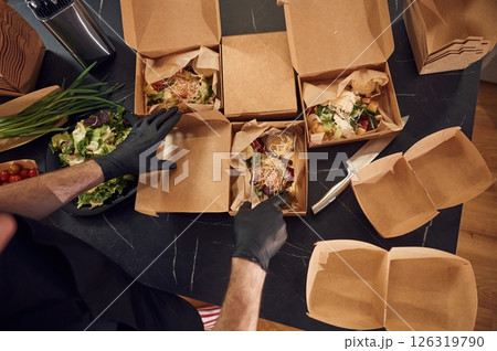 Top view. Man is packing food into the paper eco boxes. Indoors, restaurant 126319790