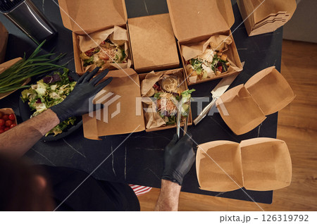Top view. Man is packing food into the paper eco boxes. Indoors, restaurant Top view. Man is packing food into the paper eco boxes. Indoors, restaurant 126319792