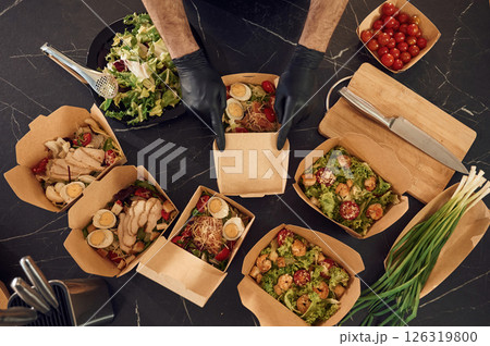 Meat, vegetables, tomatoes, eggs on the table. Man is packing food into the paper eco boxes. Indoors, restaurant Meat, vegetables, tomatoes, eggs on the table. Man is packing food into the paper eco boxes. Indoors, restaurant 126319800