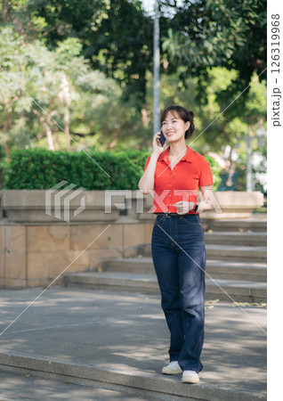 Southeast asian woman young female entrepreneur enjoys remote work as small business owner businesswoman talking on phone outdoors in park setting 126319968