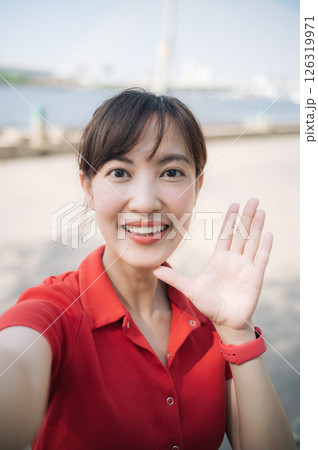 Southeast asian woman young female entrepreneur remote work small business owner businesswoman smiling outdoors taking selfie casual red shirt cheerful day Southeast asian woman young female entrepreneur remote work small business owner businesswoman smiling outdoors taking selfie casual red shirt cheerful day 126319971