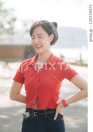 Southeast asian woman young female entrepreneur enjoys remote work as small business owner and businesswoman outdoors in casual red shirt with cheerful expression Southeast asian woman young female entrepreneur enjoys remote work as small business owner and businesswoman outdoors in casual red shirt with cheerful expression 126319972