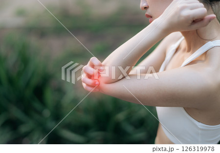 Southeast asian female teen experiencing pain during exercise while jogging running in public park, highlighting sport health concerns and discomfort in elbow area, pain in exercise concept. 126319978
