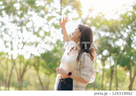 Southeast asian female young woman enjoying refreshing deep breath in public park expressing wellness and embracing healthy lifestyle in sunlight. young woman in casual attire enjoys sunny day outdoor 126319982