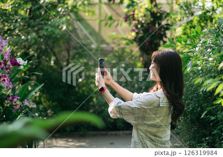 Southeast asian female young woman enjoying refreshing deep breath in public park surrounded by lush greenery and flowers embracing wellness and healthy lifestyle with joyful smile 126319984