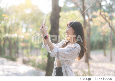 Southeast asian female young woman enjoys refreshing deep breath in public park, wellness and healthy lifestyle joyful smile on sunny day outdoor. Asian woman enjoys summer while taking selfie in park 126319990