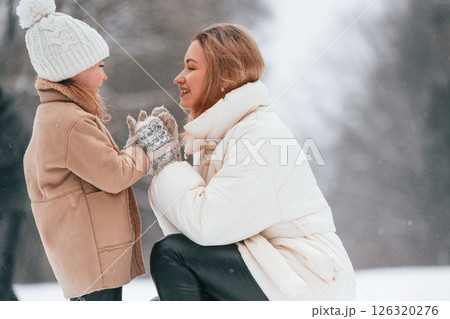 Mother with her little daughter are looking at each other and enjoying walk outdoors at winter time. Son is at background Mother with her little daughter are looking at each other and enjoying walk outdoors at winter time. Son is at background 126320276