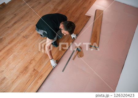 Top view. Man is installing new laminated wooden floor Top view. Man is installing new laminated wooden floor 126320423