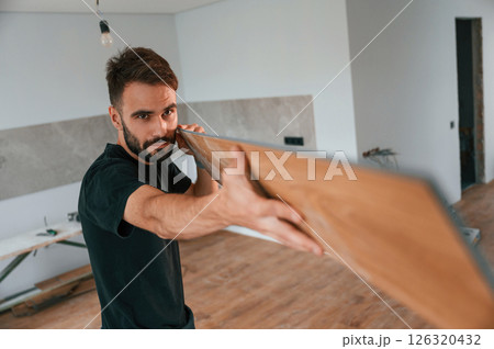 Looking at the length of the plank. Man is installing new laminated wooden floor Looking at the length of the plank. Man is installing new laminated wooden floor 126320432