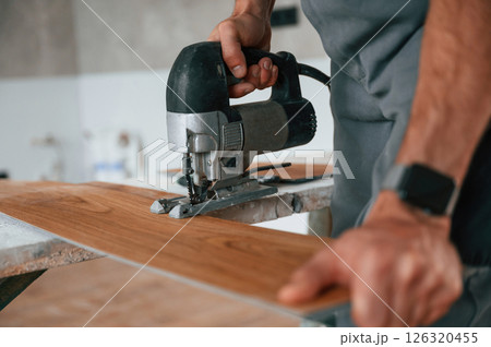 Using the electric machine tool to cut the plank. Man is installing new laminated wooden floor 126320455