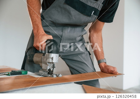 Using the electric machine tool to cut the plank. Man is installing new laminated wooden floor 126320458