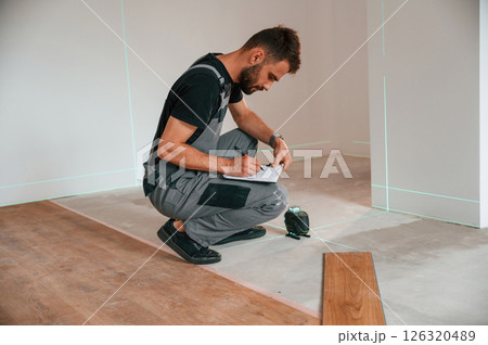Sitting and making measurements by using laser leveler. Man is installing new laminate wooden floor Sitting and making measurements by using laser leveler. Man is installing new laminate wooden floor 126320489
