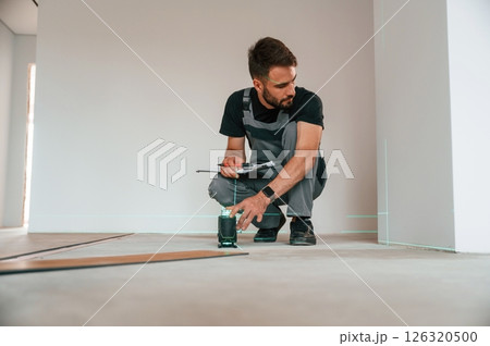 Laser leveler device. Man is installing new laminated wooden floor Laser leveler device. Man is installing new laminated wooden floor 126320500