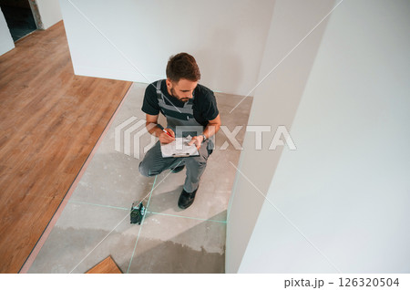 Using the device that shows straight lines by laser. Man is installing new laminated wooden floor Using the device that shows straight lines by laser. Man is installing new laminated wooden floor 126320504
