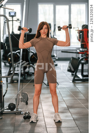 Holding dumbbells. Beautiful woman with sport body type is in the gym 126320834