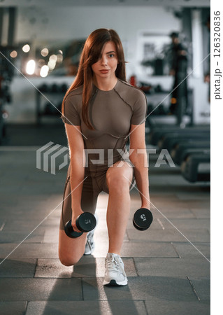 Holding dumbbells. Beautiful woman with sport body type is in the gym Holding dumbbells. Beautiful woman with sport body type is in the gym 126320836