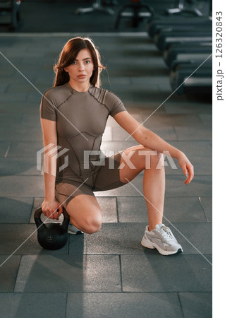 Sitting on the floor with dumbbell on it. Beautiful woman with sport body type is in the gym 126320843