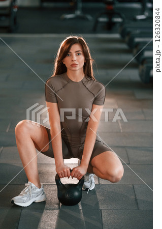 Sitting on the floor with dumbbell on it. Beautiful woman with sport body type is in the gym 126320844