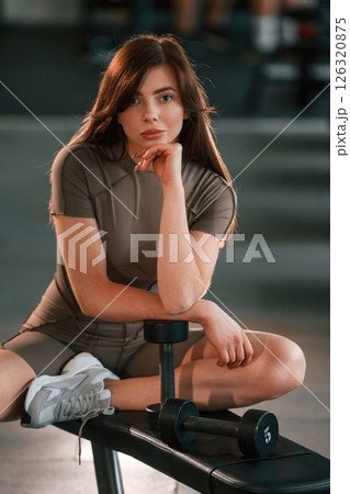 Sitting on the bench. Beautiful woman with sport body type is in the gym Sitting on the bench. Beautiful woman with sport body type is in the gym 126320875