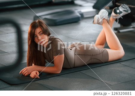 Lying down on the yoga mat and resting. Beautiful woman with sport body type is in the gym Lying down on the yoga mat and resting. Beautiful woman with sport body type is in the gym 126320881