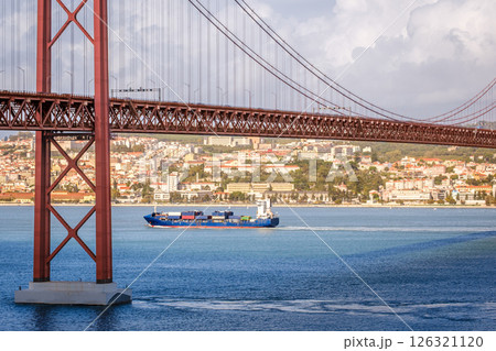 Colorful landscape with blue container ship on Tagus river under iconic 25 de Abril or 25th April bridge, Lisbon, Portugal. Famous ironwork of red suspension bridge, vibrant cityscape, urban Colorful landscape with blue container ship on Tagus river under iconic 25 de Abril or 25th April bridge, Lisbon, Portugal. Famous ironwork of red suspension bridge, vibrant cityscape, urban 126321120