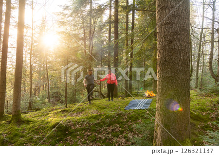 Couple enjoying a romantic walk in a serene forest at sunset, surrounded by lush greenery and soft golden light filtering through trees 126321137