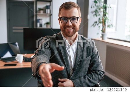 Giving the hand, greetings gesture. Businessman in suit is in the office with computer 126321549